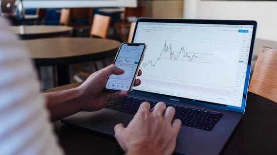 A user examines prices on a mobile phone while looking at a graph on a laptop